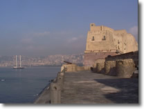 castel dell'ovo visto dal pontile. In lontananza è visibile parte del panorama della città di napoli ed una barca a vela in mezzo al mare