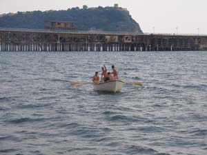 una barca a remi in mezzo al mare, con sullo sfondo un molo