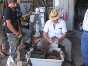 un uomo anziano lavora con le mani mentre un ragazzo, accanto a lui, lo osserva