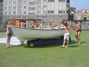 un uomo ed un gruppo di ragazzi, in costume da bagno, intorno ad una barca sulla terraferma