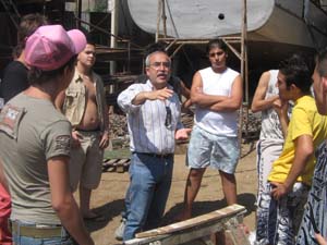 un uomo, in piedi, parla ad un gruppo di ragazzi all'interno di un cantiere