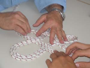 quattro mani su un tavolo dispongono una corda in modo da formare dei nodi