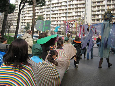 bambini in fila che rappresentano un serpente tra bandiere e maschere