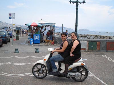 due donne sullo scooter e sullo sfondo un chiosco di bibite